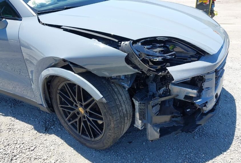 一輛灰色保時捷Cayenne前部嚴重受損的事故車，右前大燈破碎，保險桿變形脫落，引擎蓋損壞。車事通提供專業的保時捷Cayenne事故車評估與高價收購服務，24小時全台到府服務。