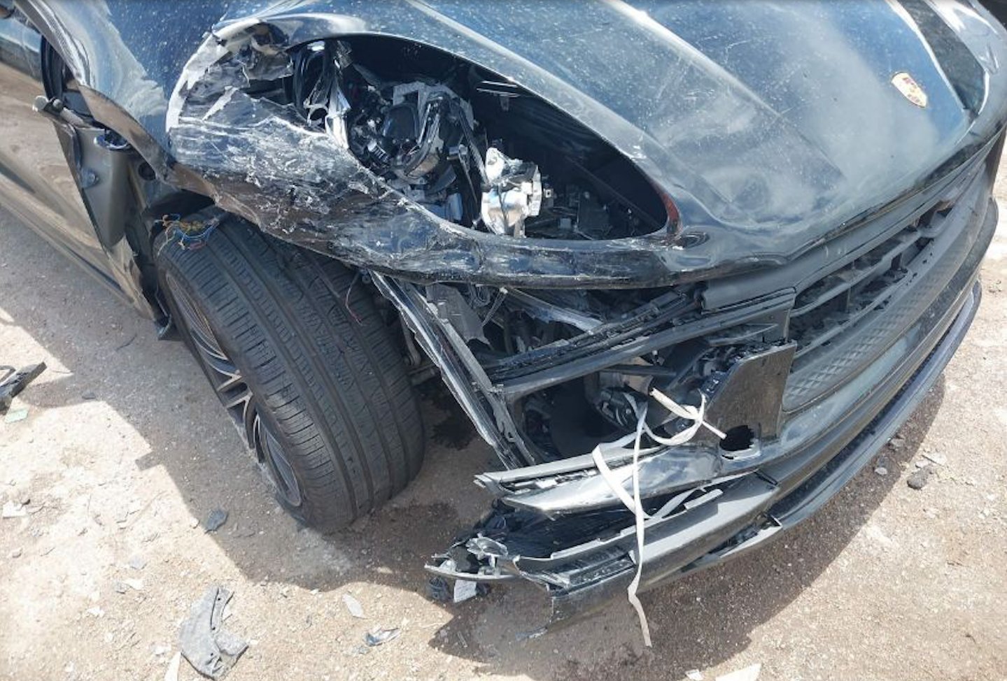 一輛深灰色保時捷Macan SUV前部嚴重受損的事故車,前保險桿完全損毀,引擎蓋變形,左前大燈破損,前擋風玻璃裂痕明顯。車事通提供專業的保時捷Macan事故車評估與高價收購服務,24小時全台到府評估。