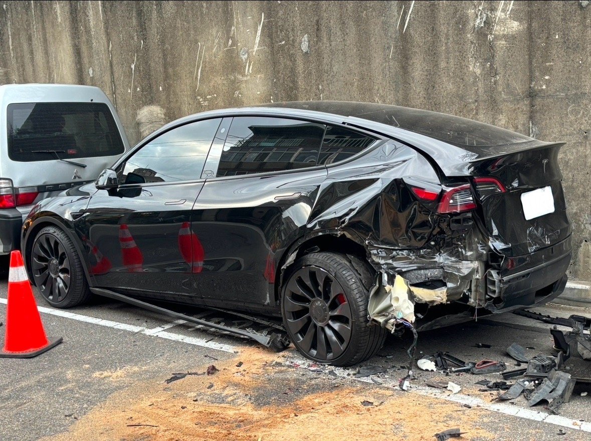一輛黑色Tesla Model Y電動休旅車發生嚴重側面撞擊事故，右側車身嚴重變形凹陷，車門損毀，車窗破碎，輪圈受損，現場散落大量碎片。車事通提供Tesla Model Y電動車事故專業評估、電池系統檢測、高壓電路安全檢測與高價收購服務，全台24小時專業處理電動車嚴重事故案例。