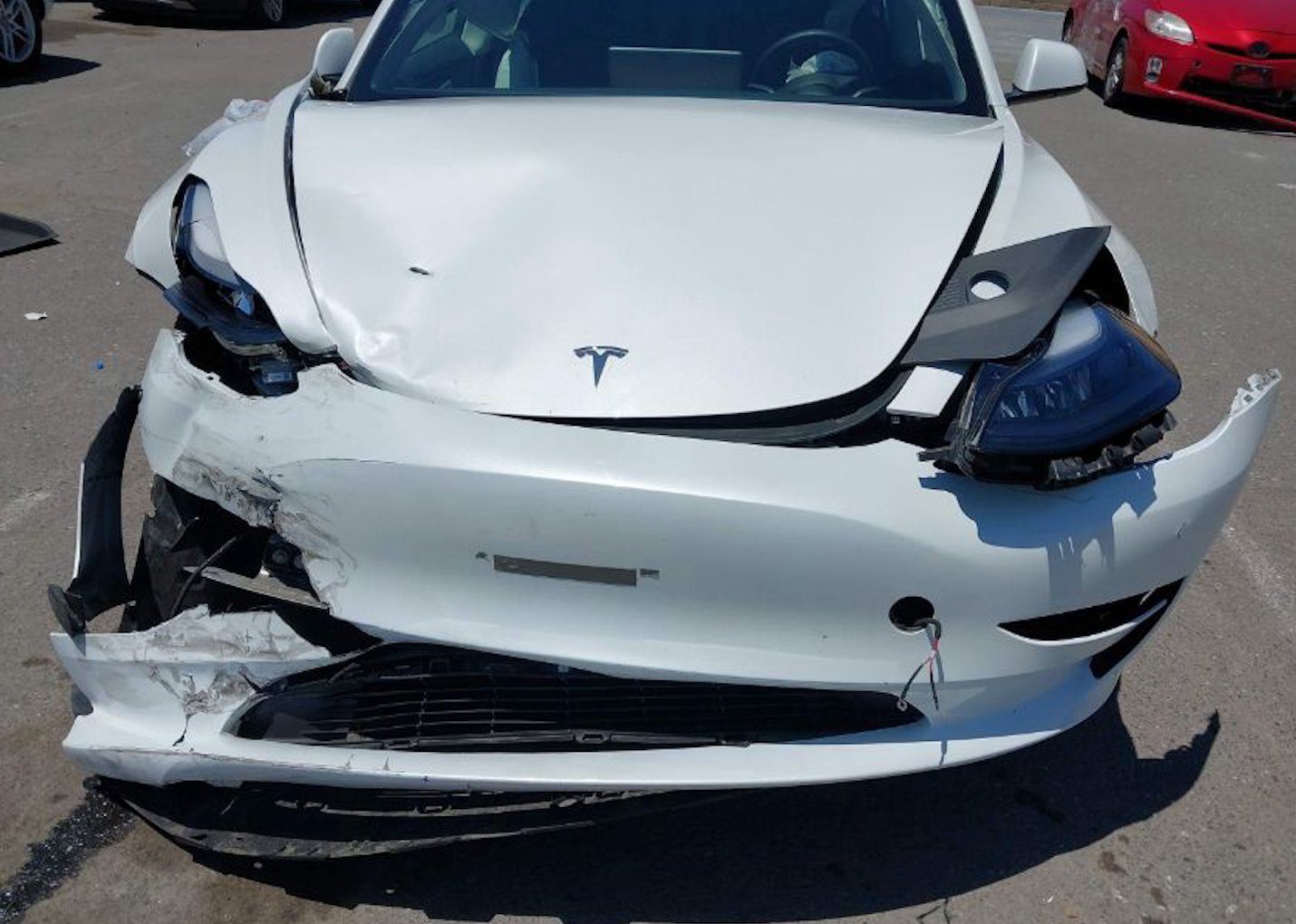 一輛白色特斯拉Model 3前端嚴重撞擊事故車，前保險桿完全脫落變形，左右大燈總成破損，引擎蓋大幅凹陷。車事通提供專業的特斯拉Model 3事故車損傷評估與高價收購服務，具備電動車專業檢測能力。