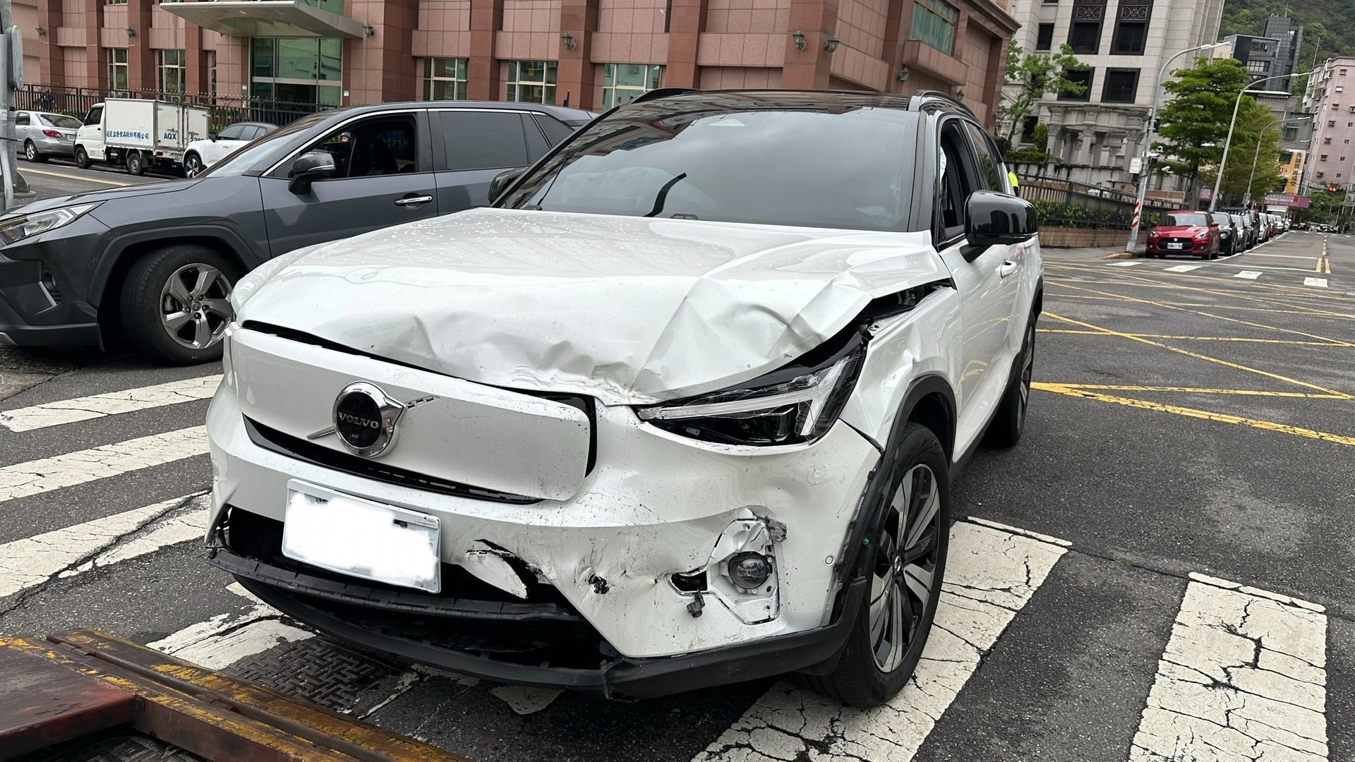 一輛白色Volvo XC40 Recharge電動休旅車發生嚴重前端撞擊事故，前保險桿嚴重變形、引擎蓋隆起變形、頭燈受損、前擋風玻璃出現裂痕，具有Volvo標誌性的雷神之錘LED日行燈設計。車事通提供Volvo電動車事故專業評估、電池系統安全檢測、高壓電路檢測與高價收購服務，全台24小時專業處理電動休旅車嚴重事故案例。